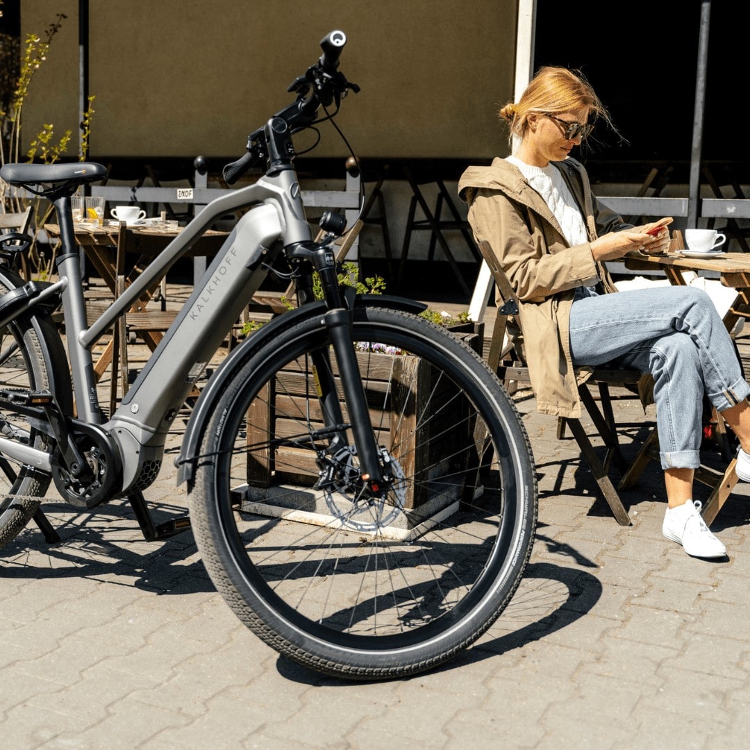 Frau sitzt vor einem Cafe, ihr Kalkhoff City E-Bike steht daneben