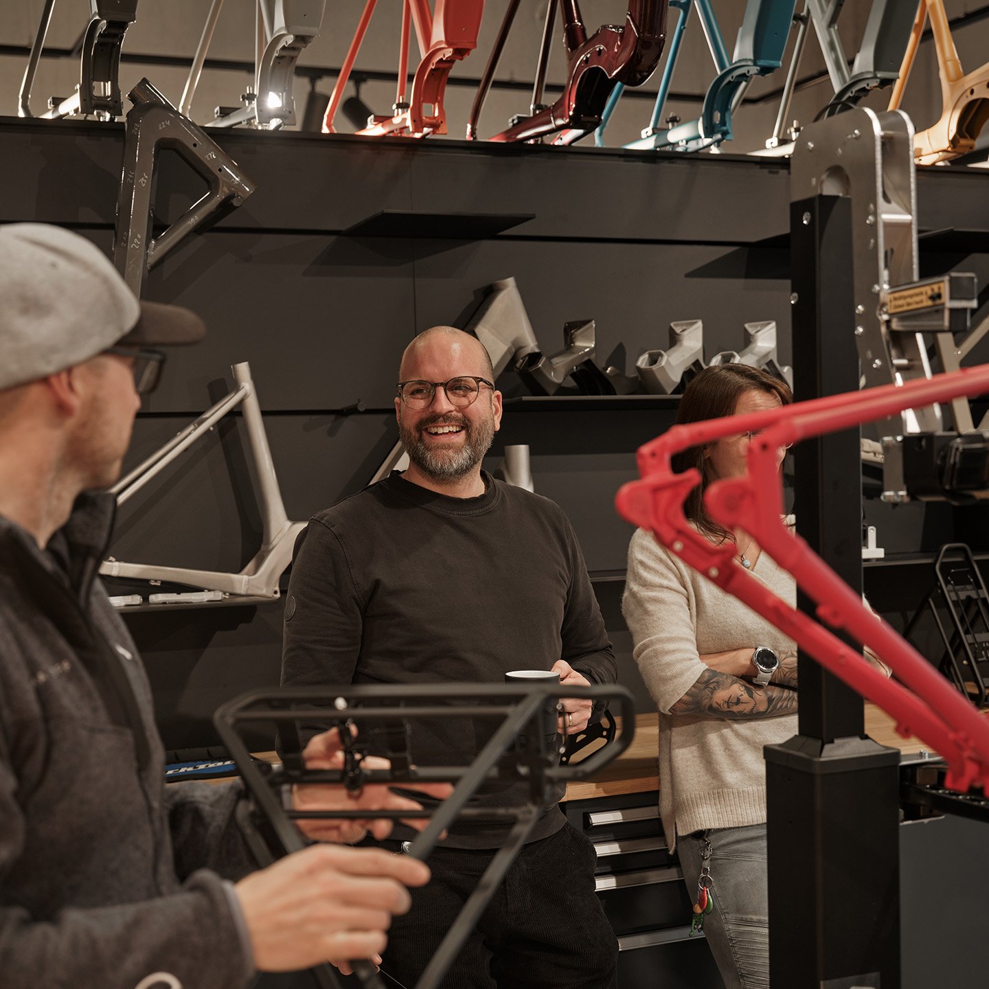 Personen in einer Werkstatt, die sich unterhalten, hinter ihnen werden verschiedene Rahmenmodelle an der Wand ausgestellt.