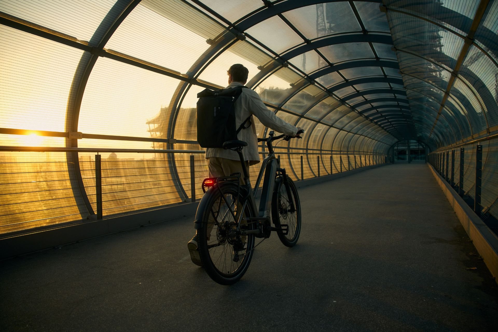 Mann geht mit Rucksack und Kalkhoff E-Bike durch eine Tunnelbrücke