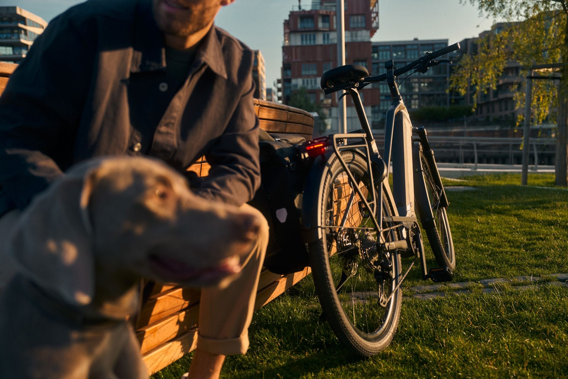 Kalkhoff E-Bike perfekt für einen Ausflug Ein Mann sitzt mit seinem Hund auf einer Bank. Neben dem Mann steht im Sonnenuntergang ein Kalkhoff E-Bike, welches im Fokus liegt.