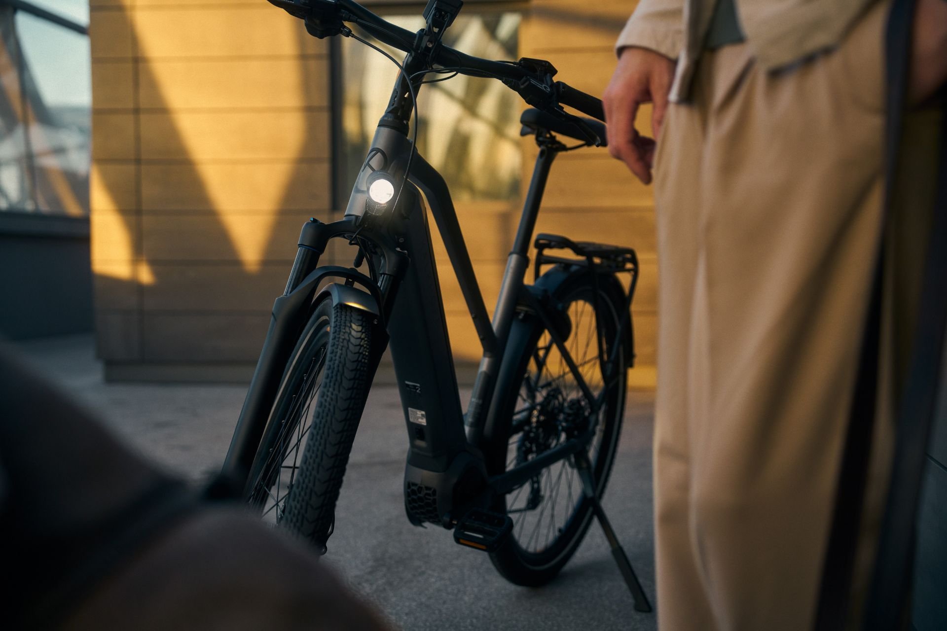Welches E-Bike passt zu mir? Eine Person steht neben einem eleganten schwarzen E-Bike auf einer sonnenbeschienenen Straße in der Stadt.