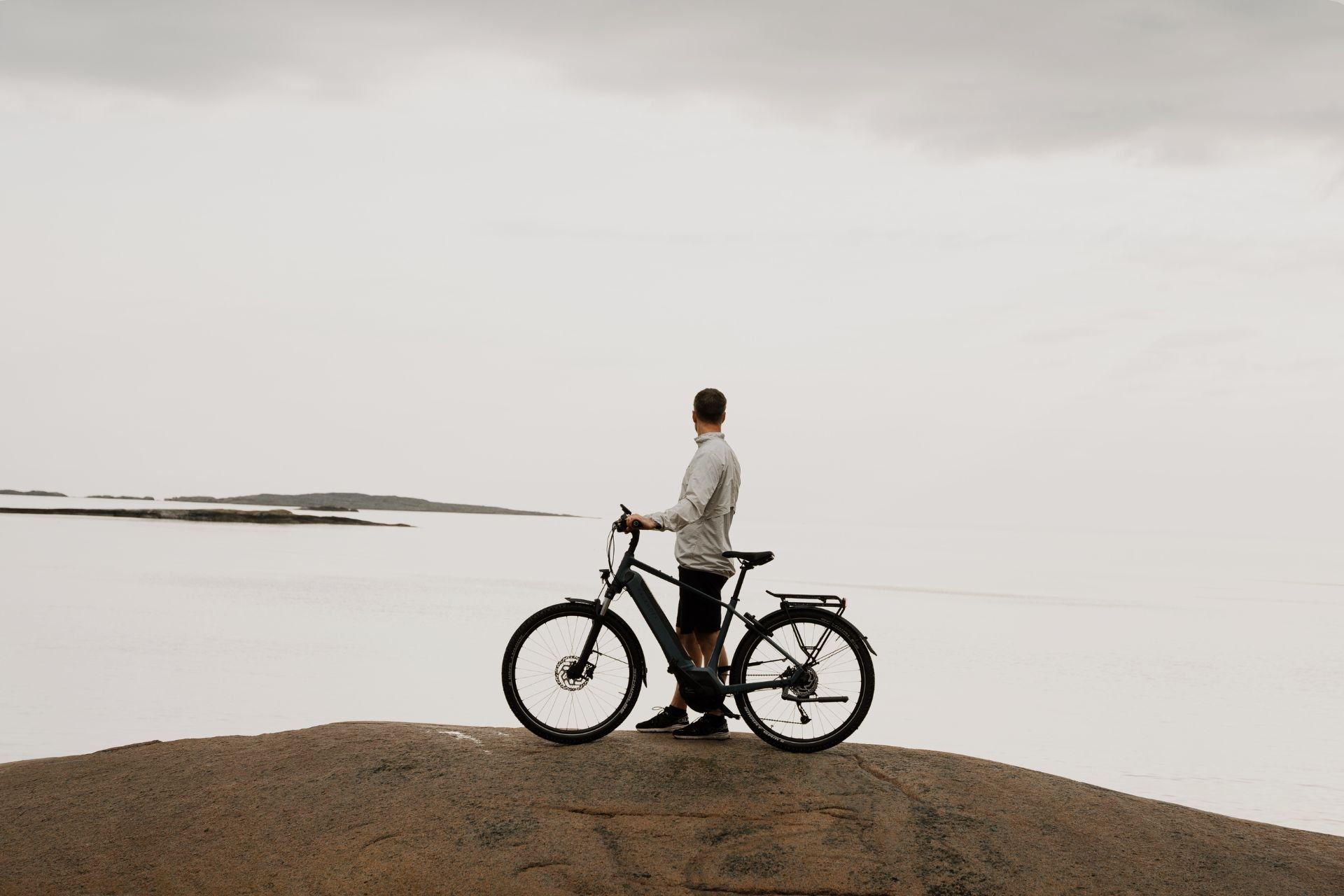 Mann steht auf einem großen Felsen und hält dabei sein Kalkhoff E-Bike in der Hand. Er schaut in Richtung Wasser, welches hinter im zu sehen ist.