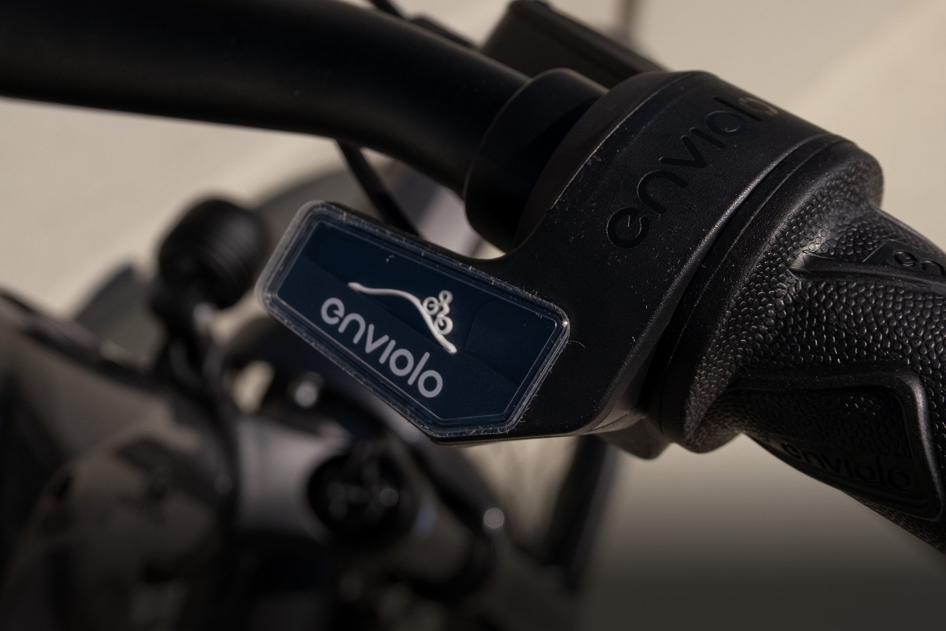 Neben Kettenschaltungen sind Nabenschaltungen die am weitesten verbreitetste Schaltungsart am Fahrrad. Close-up of a bicycle handlebar with a black Enviolo gear shifter and textured grip, featuring the Enviolo logo on a dark-blue background.