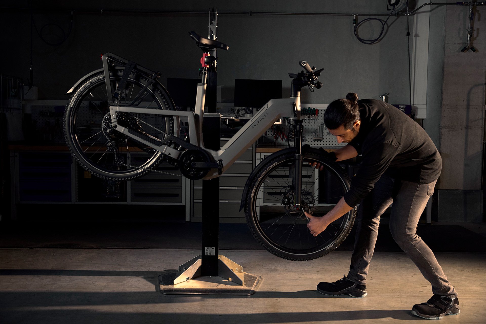 Person, die das Vorderrad eines auf einem Reparaturständer montierten E-Bikes in einer Werkstatt einstellt.