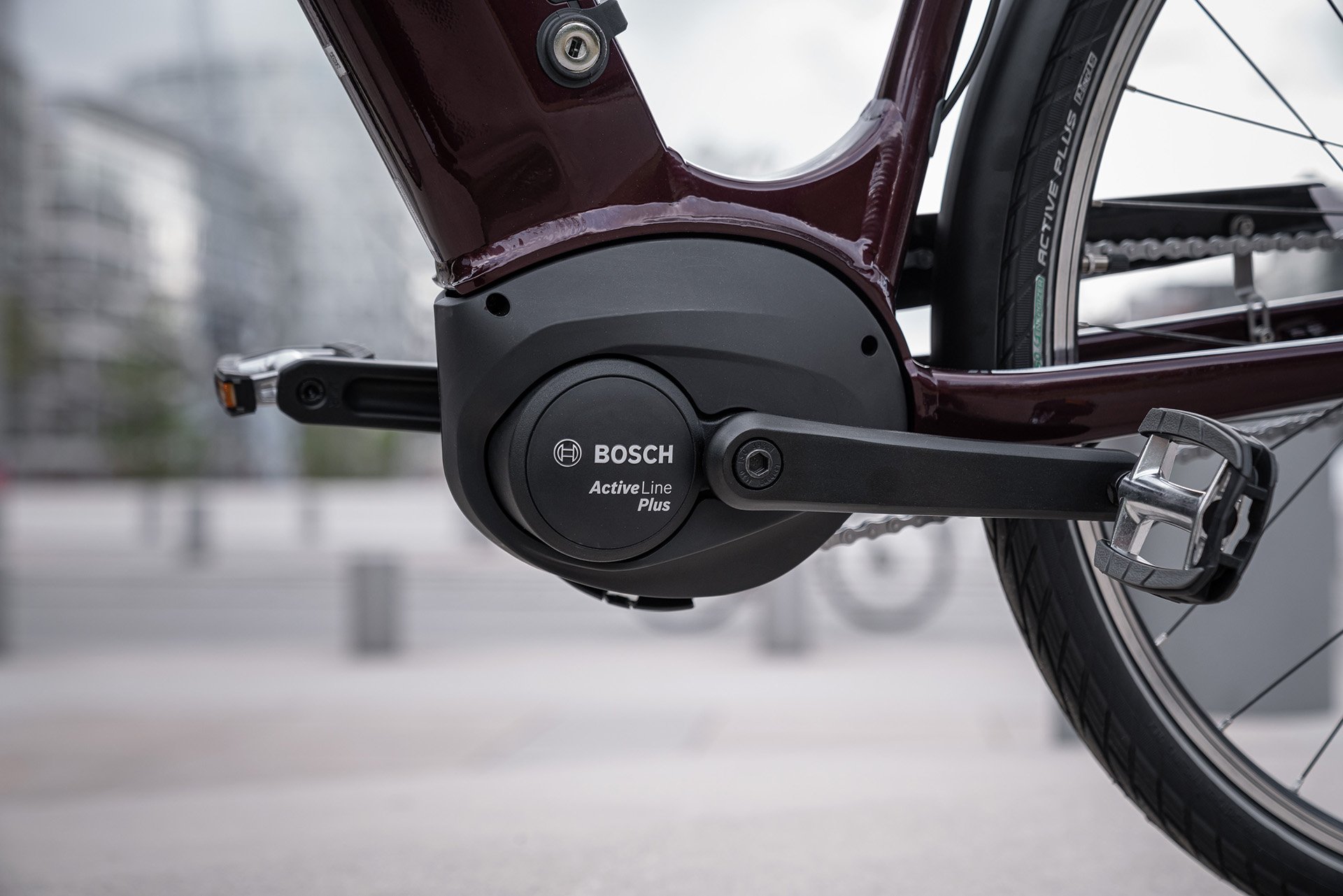 Close-up of a Bosch Active Line Plus motor on a bicycle, with a sleek frame and pedal, set in an urban outdoor environment.