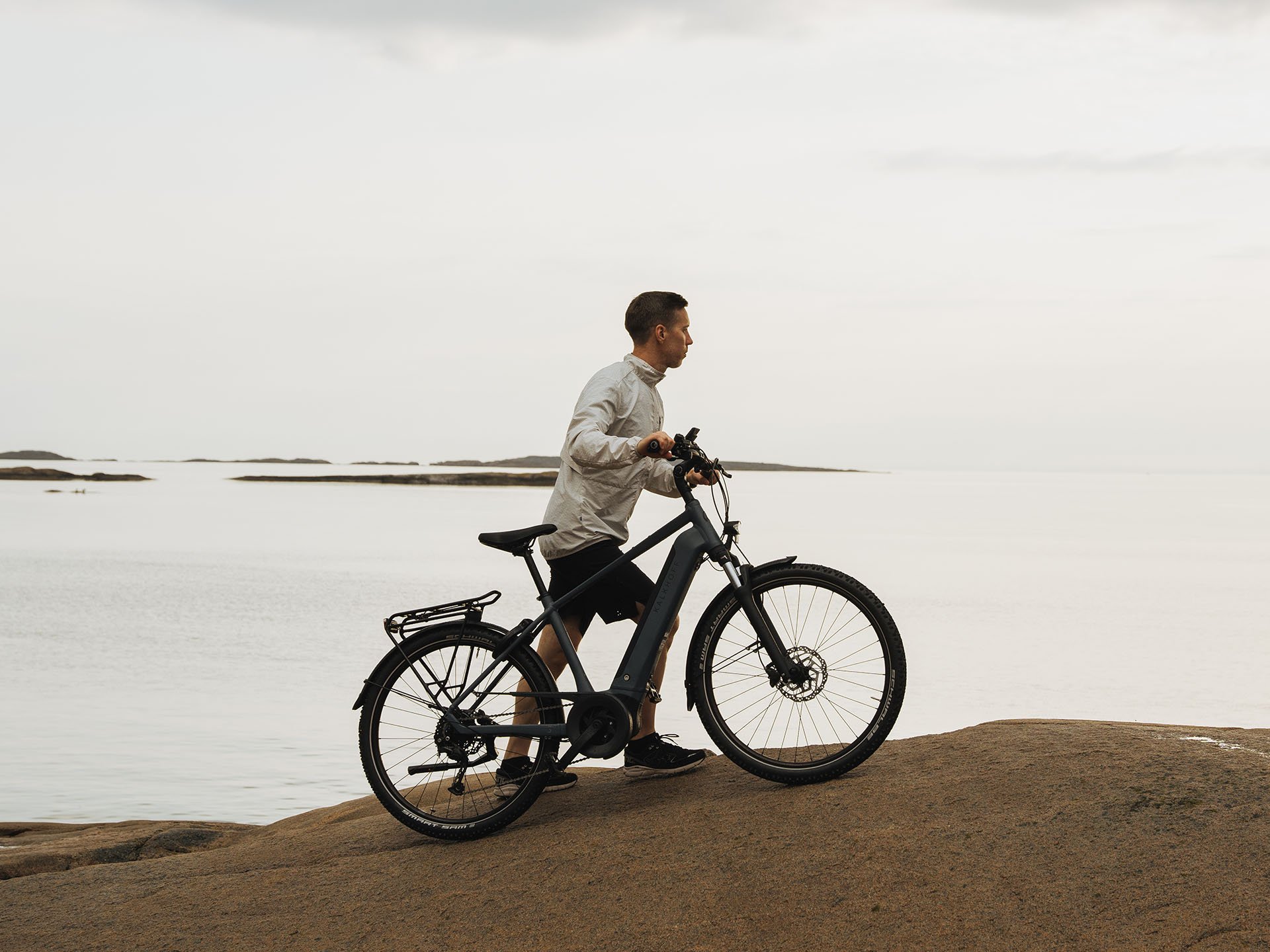 Mann schiebt sein Kalkhoff Bike am Meer einen großen Stein hoch