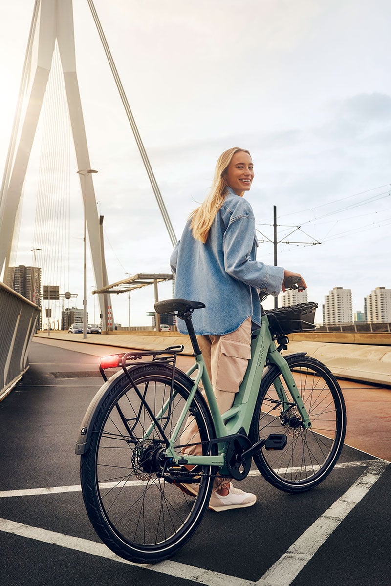 Frau steht auf einer Straßenbrücke mit ihrem Kalkhoff Image Light E-Bike und lächelt in die Kamera