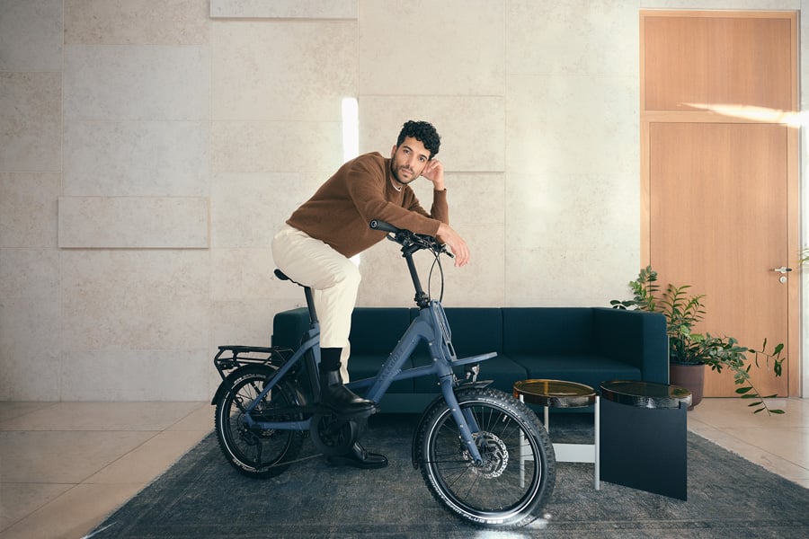 Mann lehnt sich ganz lässig an sein Kalkhoff Compact Bike in einem Wohnzimmer